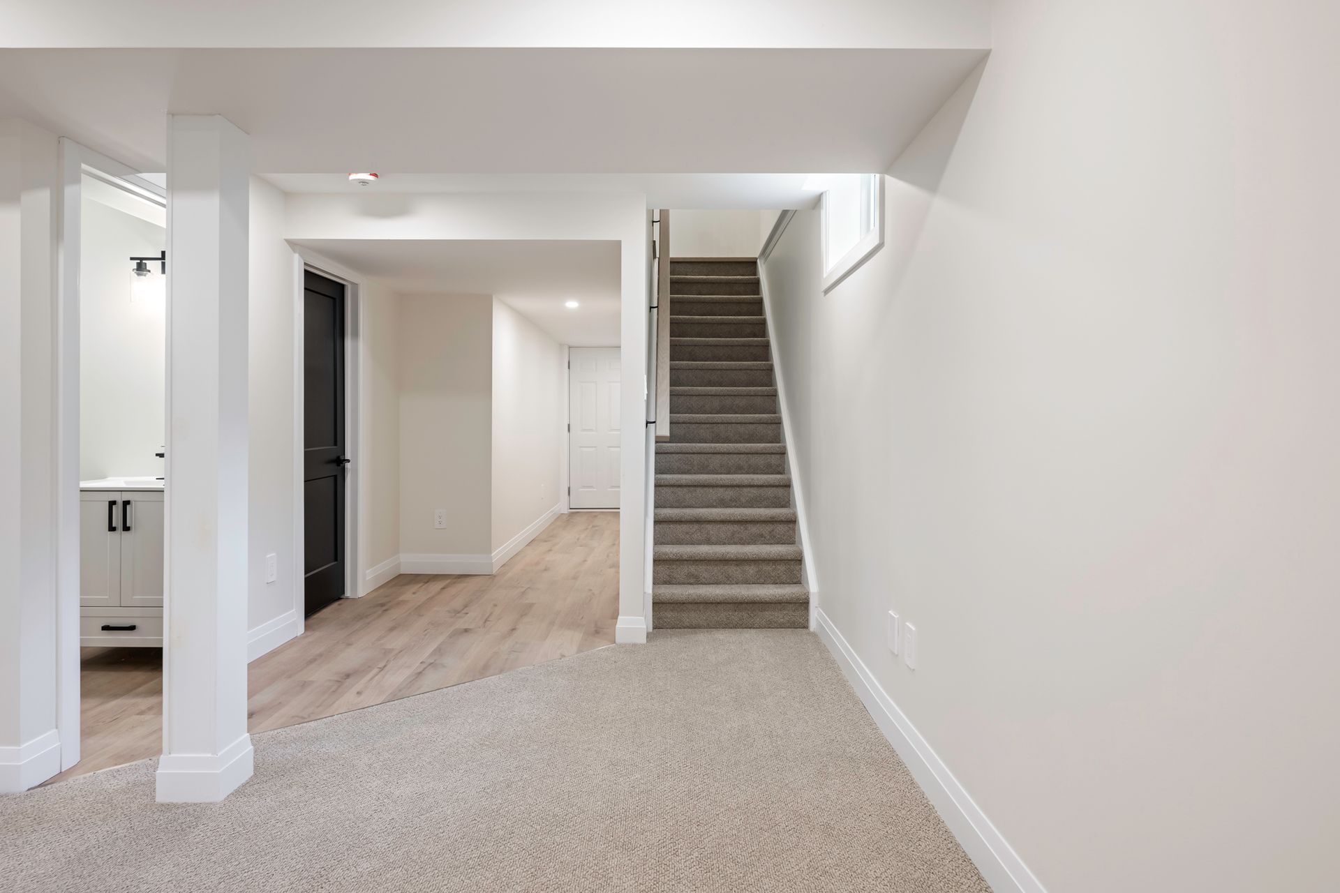 Basement interior with carpet, stairs, support columns, and white walls.