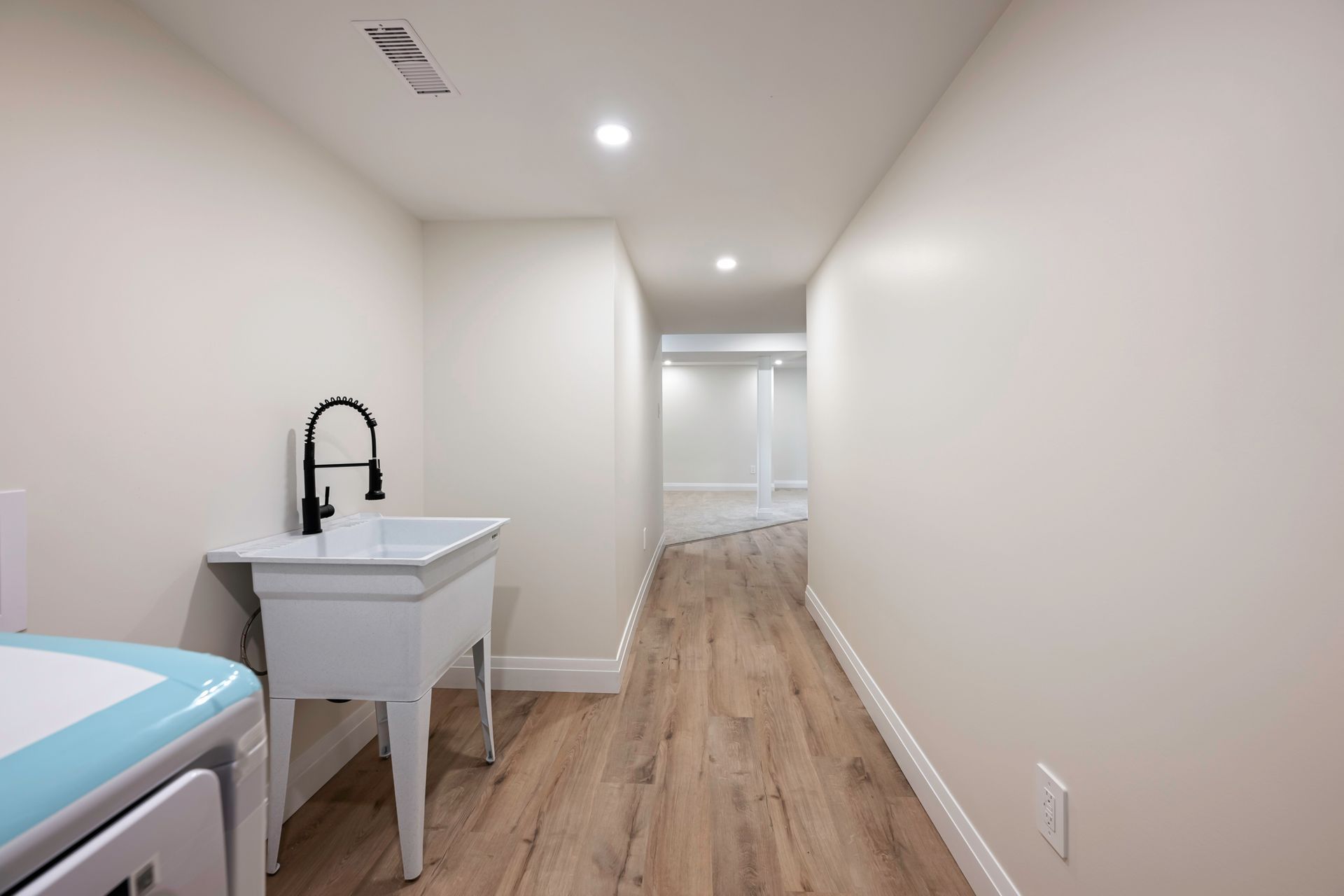 Laundry room with white walls, wood-look floor, sink with black faucet, and a light blue washing machine.