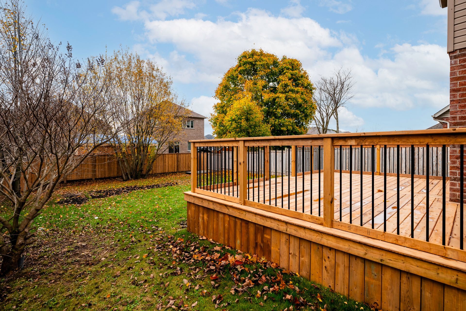 Wooden deck with black railings in backyard, autumn leaves on the lawn.