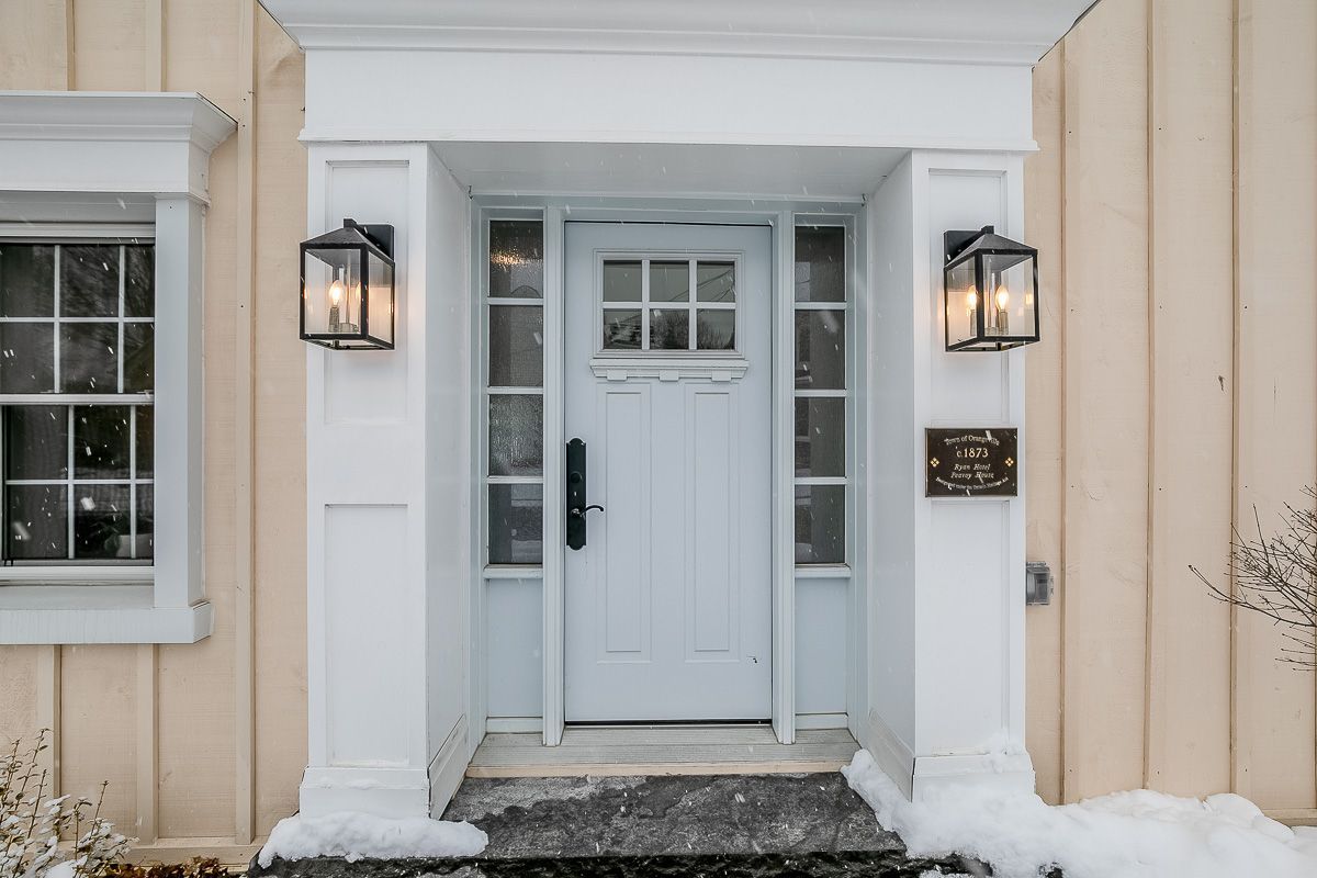 White front door with sidelights, two lanterns, and a snow-covered porch.