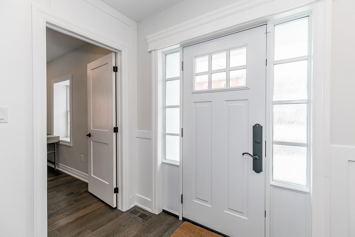 White entryway with a paneled front door flanked by sidelights and a doorway to another room.