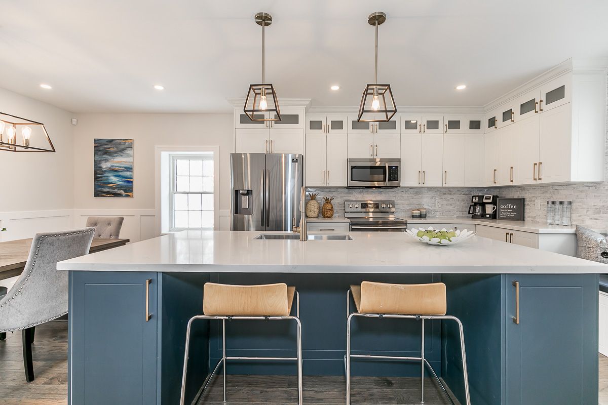 Modern kitchen with blue island and white cabinets. Two pendant lights hang over the island.