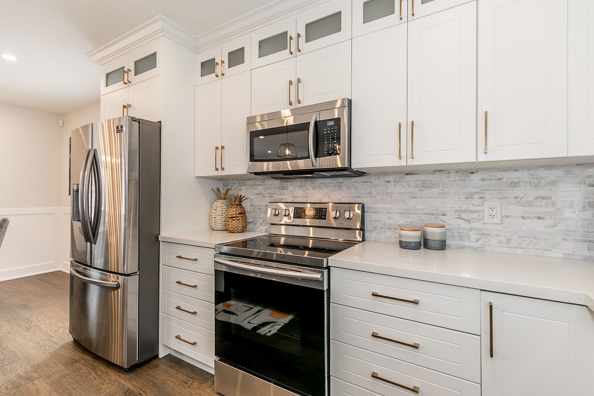 White kitchen with stainless steel appliances, white cabinets, and light backsplash.