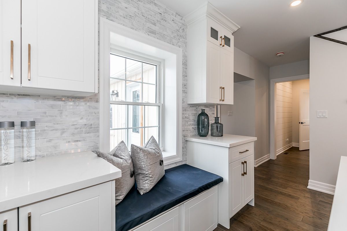 White kitchen with window seat, navy cushion, gray accent wall, and dark wood floor.