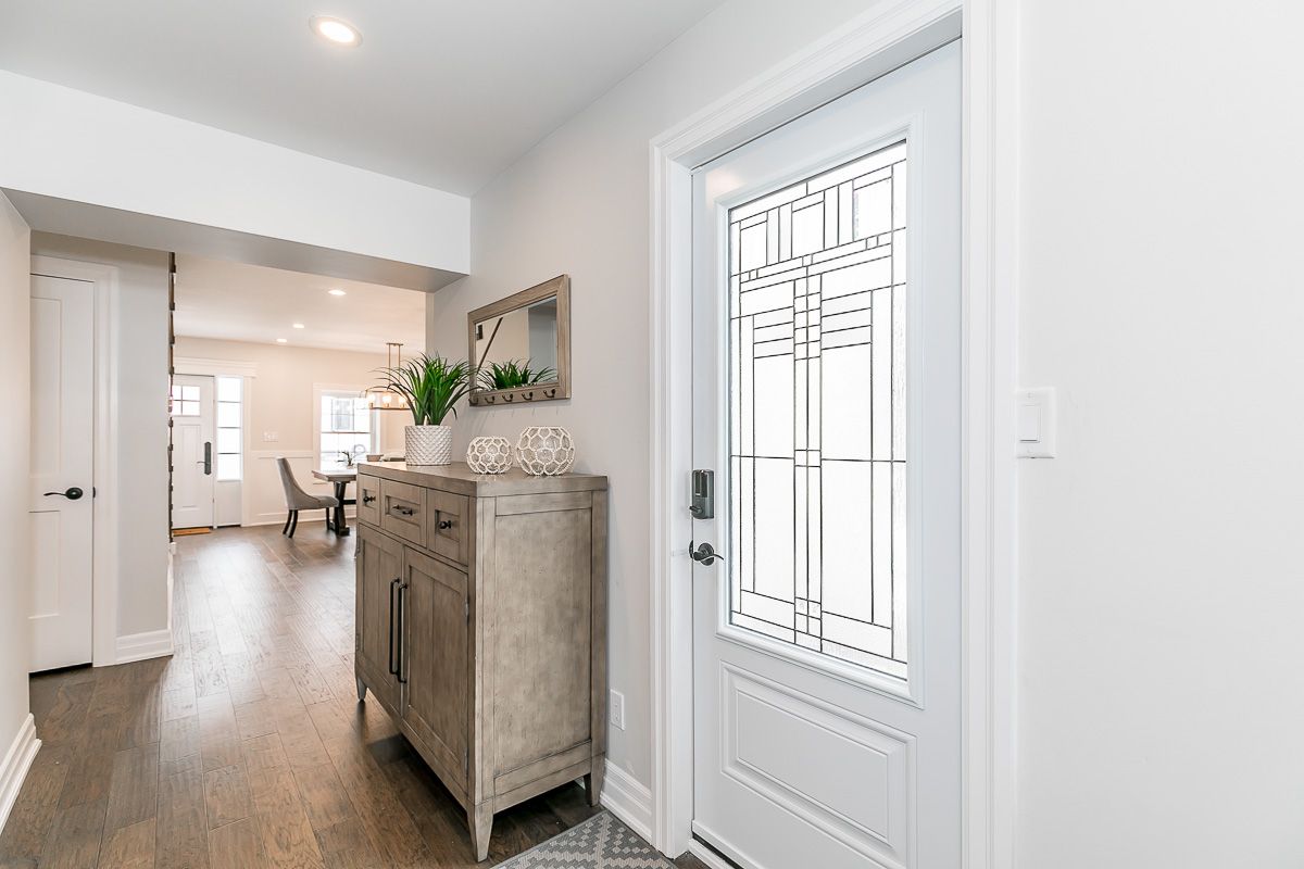 Entryway with white door, wood flooring, grey cabinet, mirror, and open doorway to dining area.