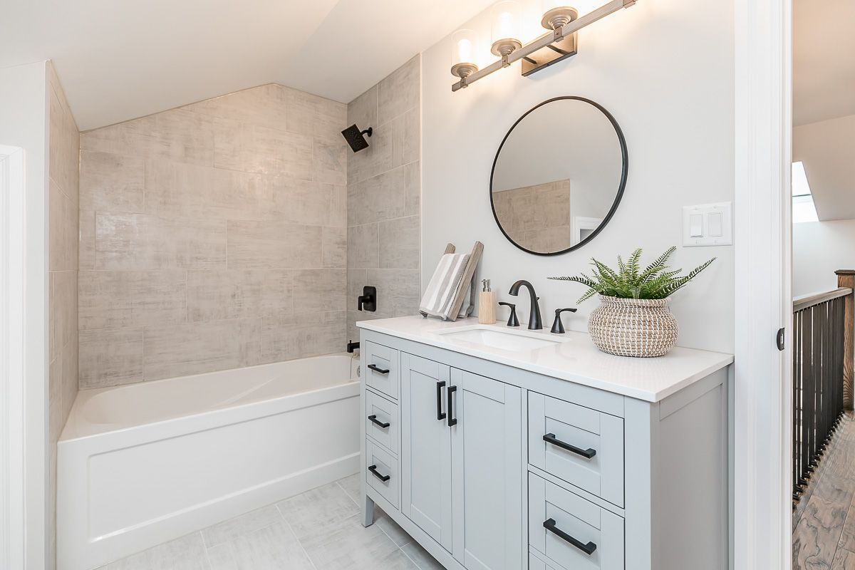 Bathroom with light blue vanity, round mirror, and tiled shower area.