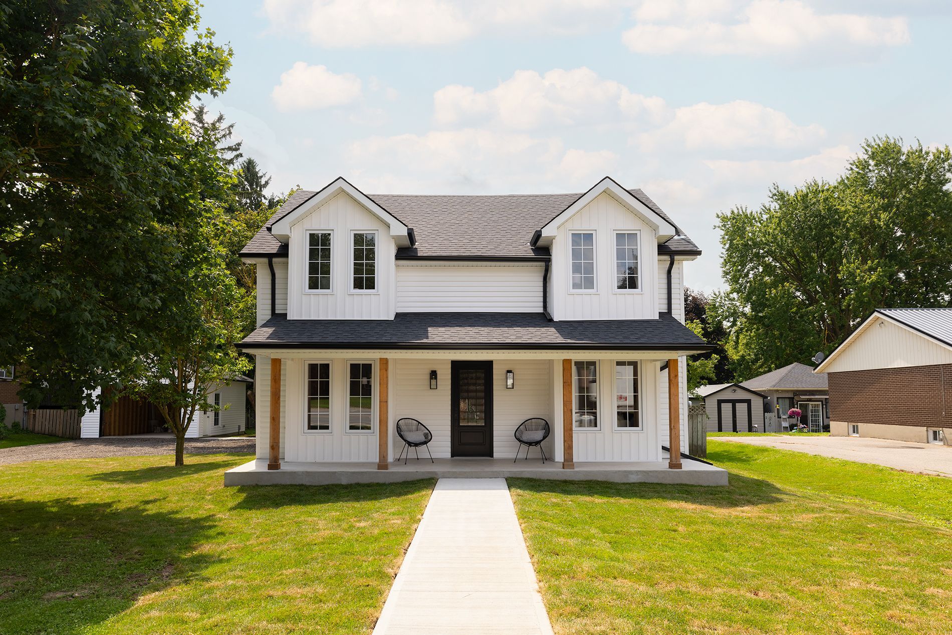 White two-story house with black roof, front porch, and walkway on green lawn under a blue sky.