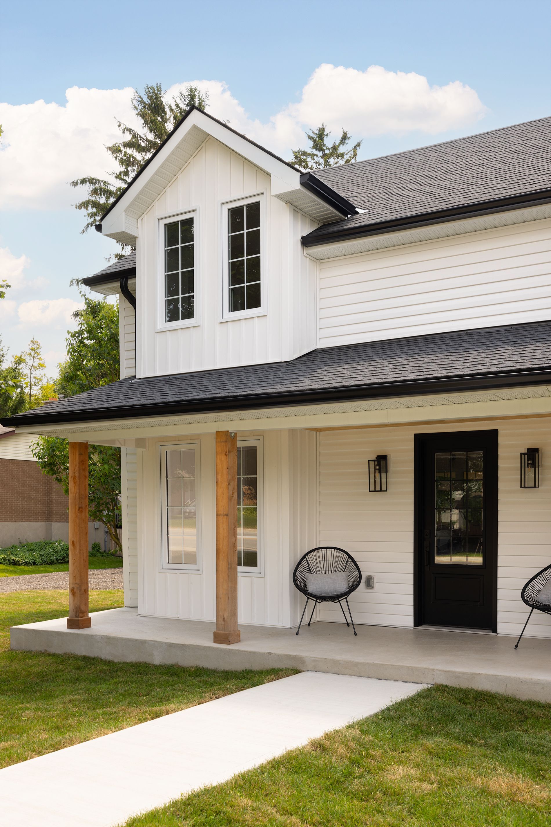 White farmhouse with black trim, porch, and walkway on a sunny day.