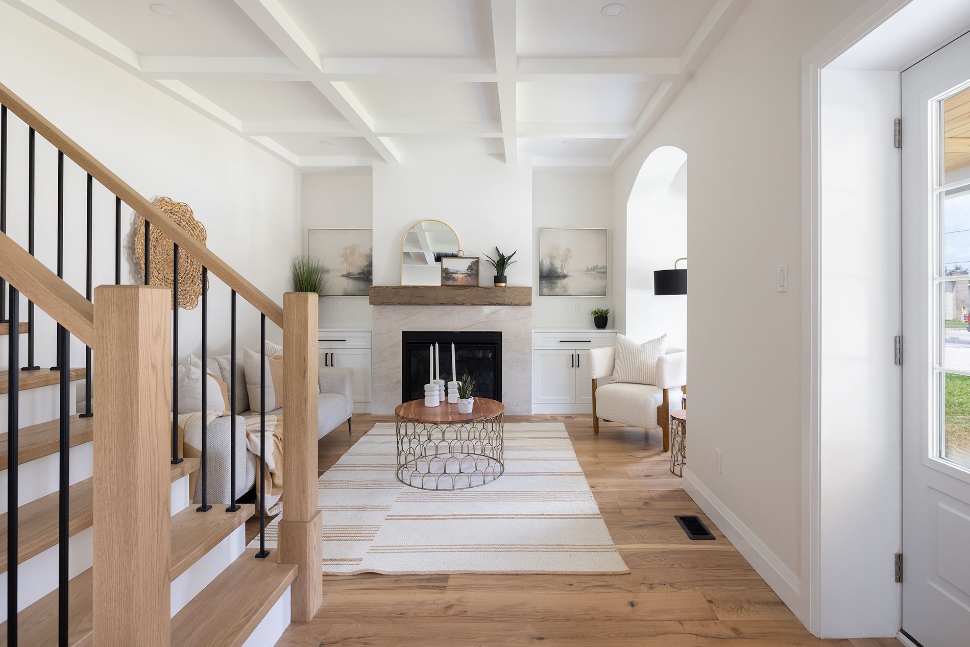 Living room with a fireplace, light wood floors, and stairway with black and wood railing.
