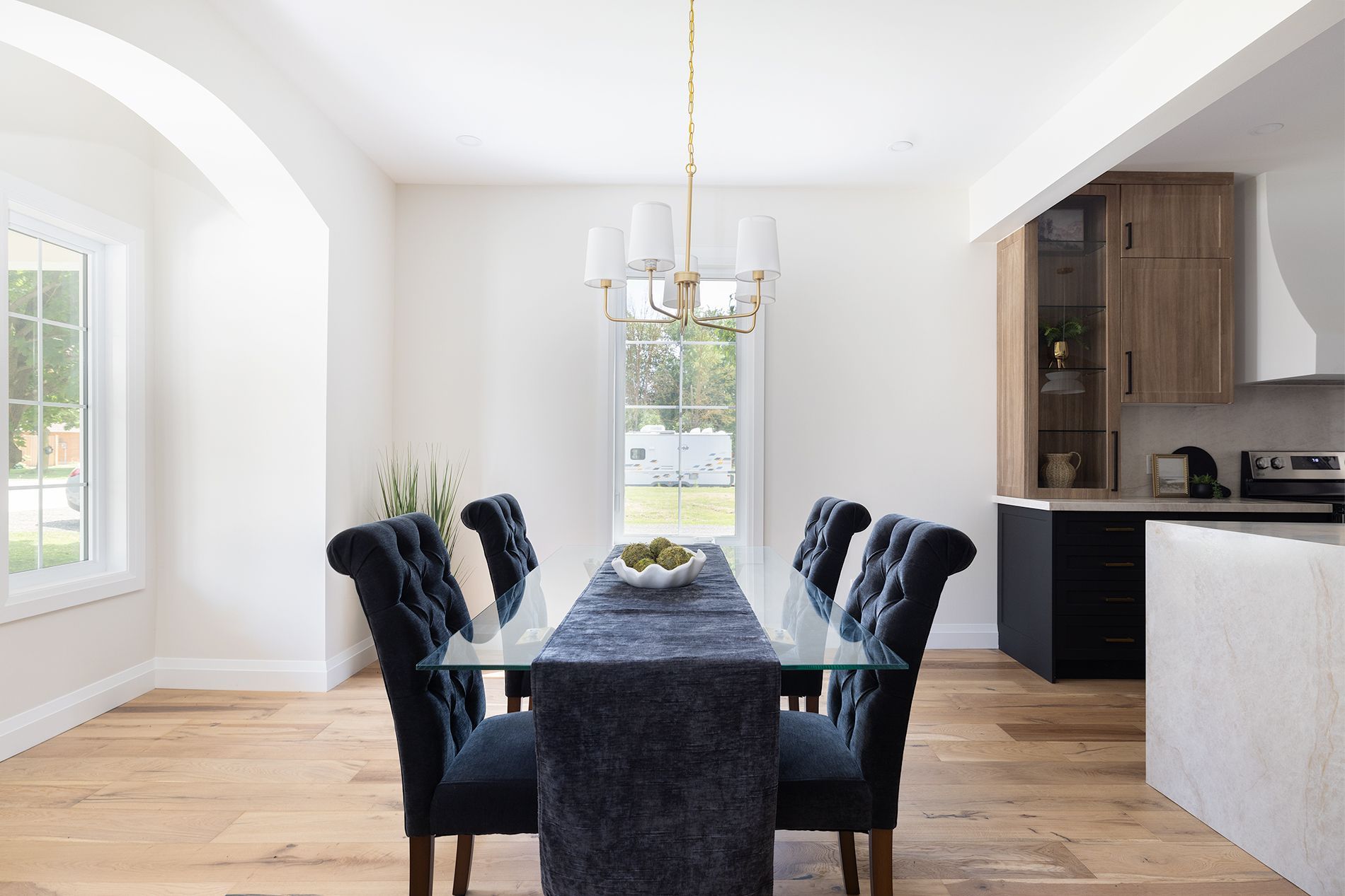 Dining room with glass table, blue velvet chairs, hardwood floor, and a view into the kitchen.