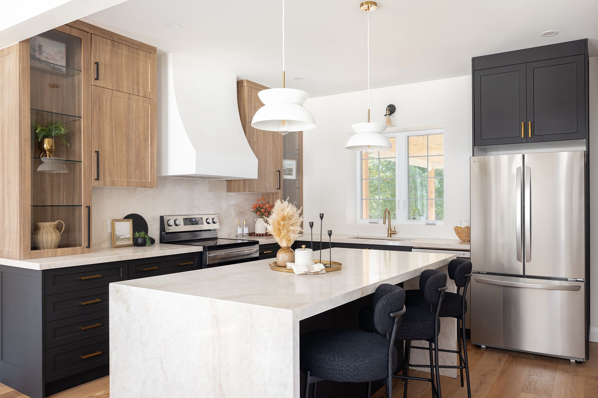 Modern kitchen with white countertops, black and wood cabinets, stainless steel refrigerator, and island with bar stools.