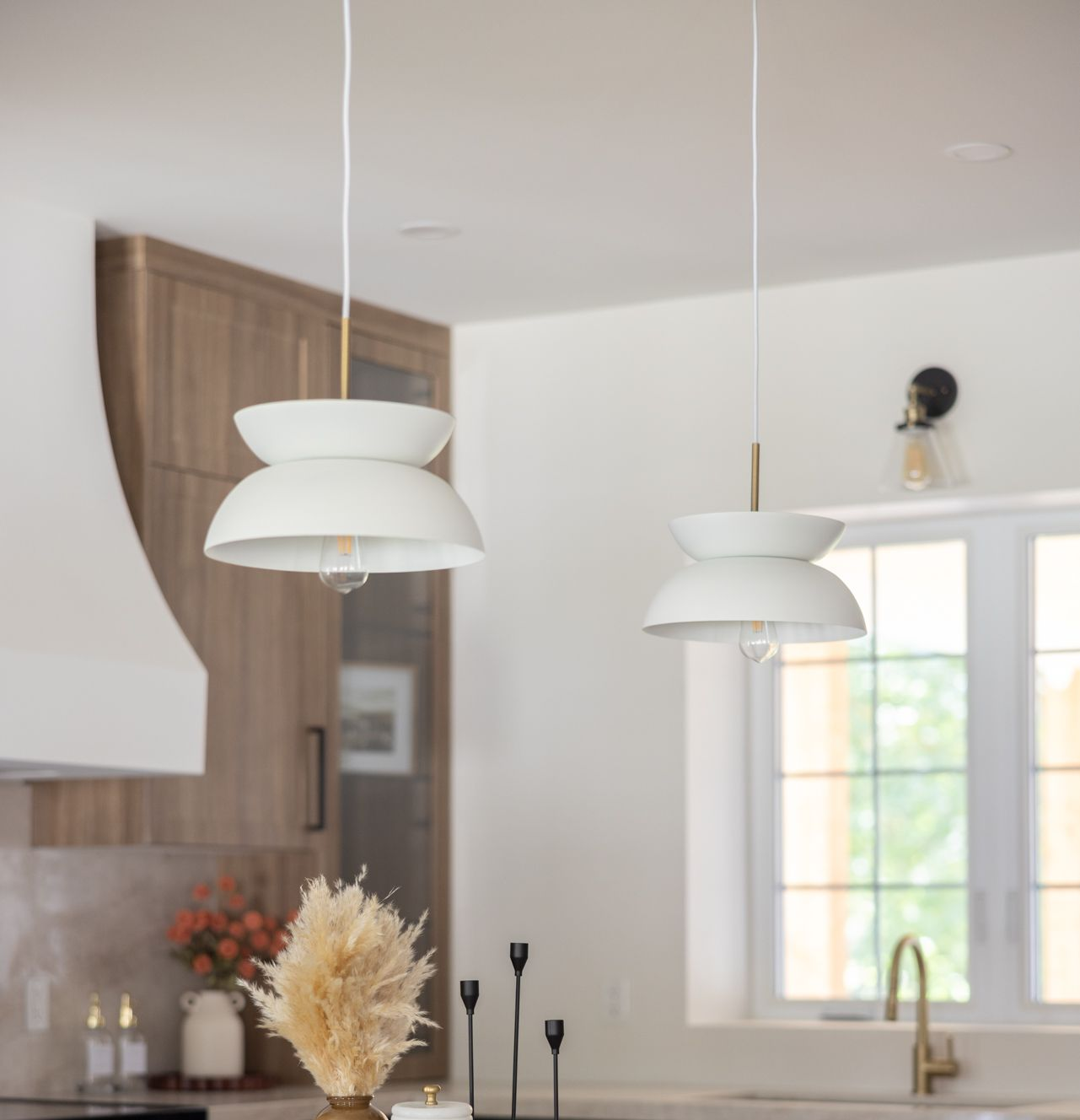 Two white pendant lights over a kitchen island, with a light-colored window and cabinetry in the background.