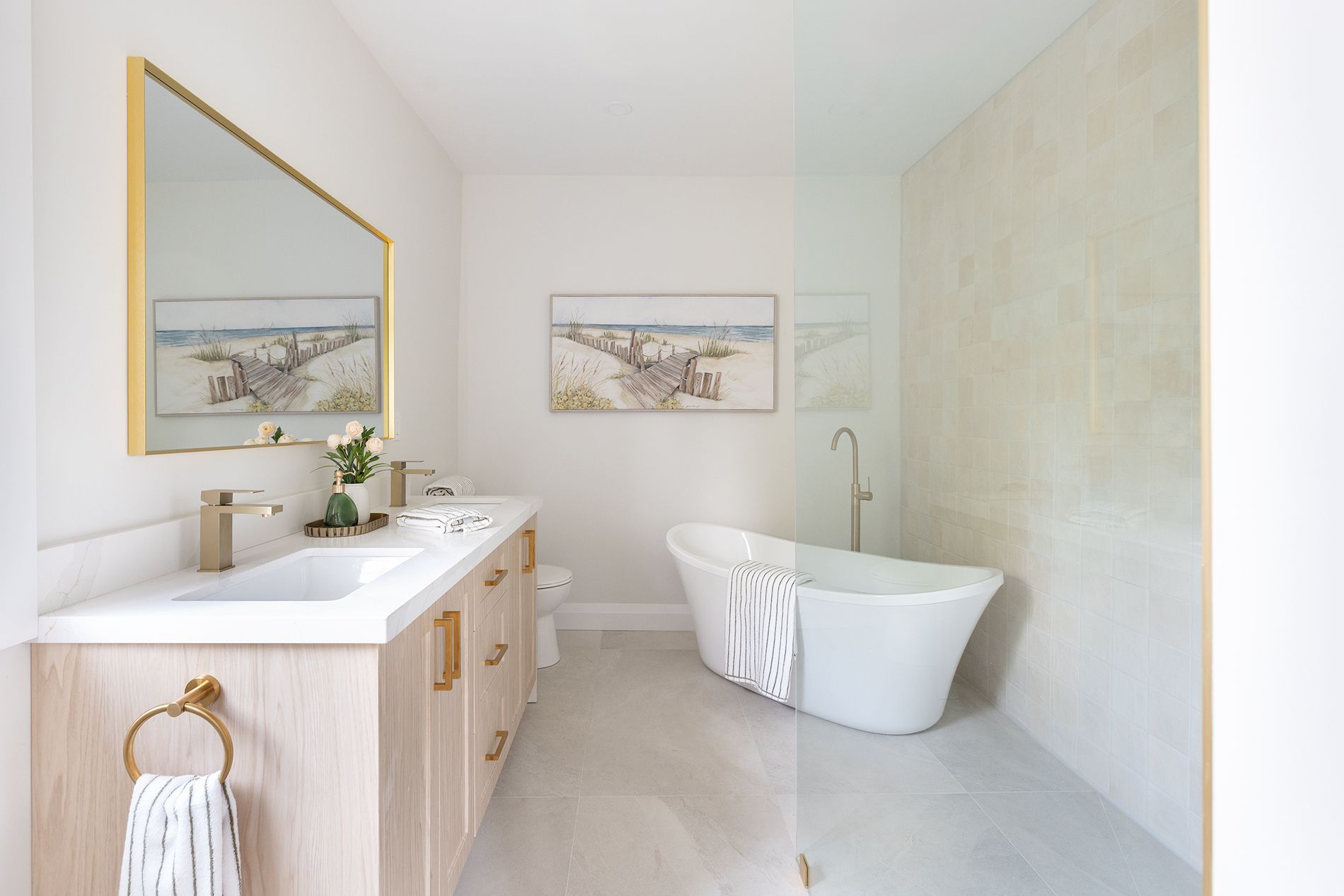Bathroom with a freestanding tub, light wood vanity, and gold accents.