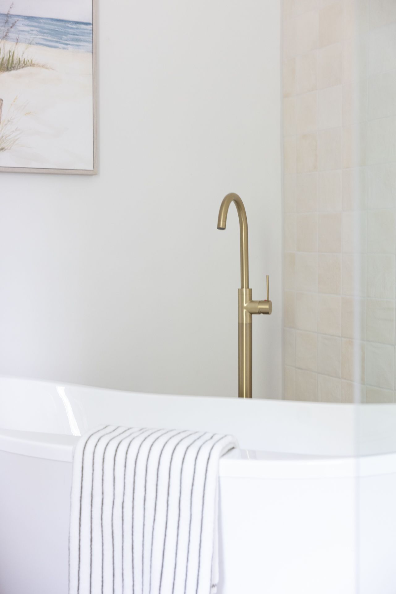 White bathtub with gold faucet; striped towel draped on side.