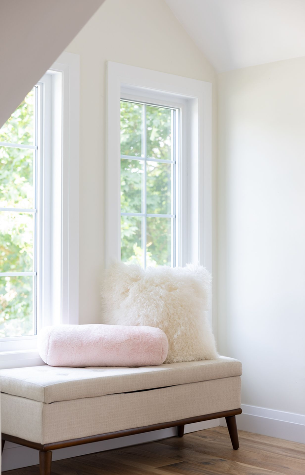 Window seat with cushions in a bright room. Light walls, beige bench, two pillows (pink and white).