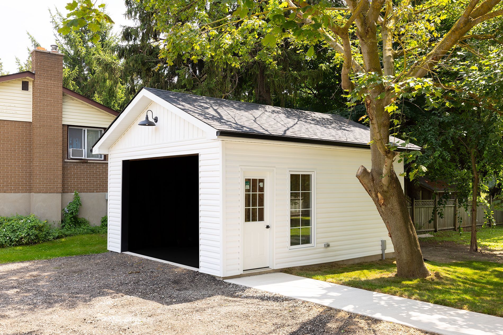 White garage with black door, small window, and concrete path, under trees.