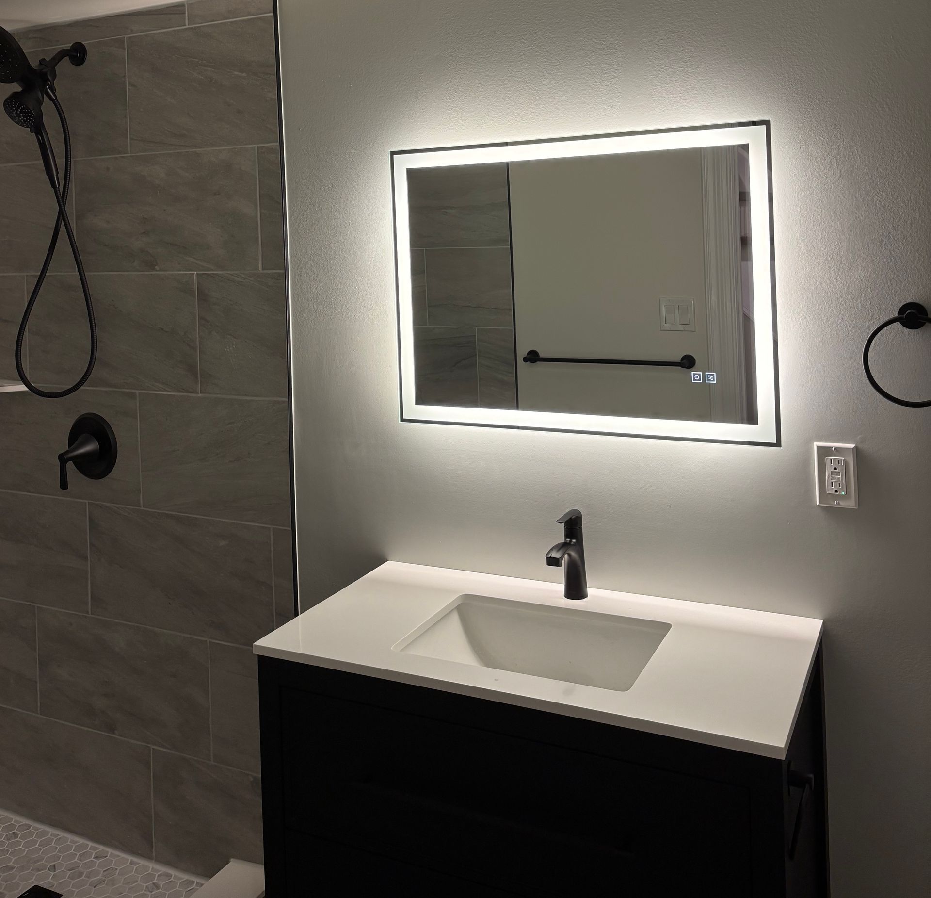Bathroom with white walls, black fixtures, and a white vanity. Light wood-look flooring. Open doorway to adjacent room.