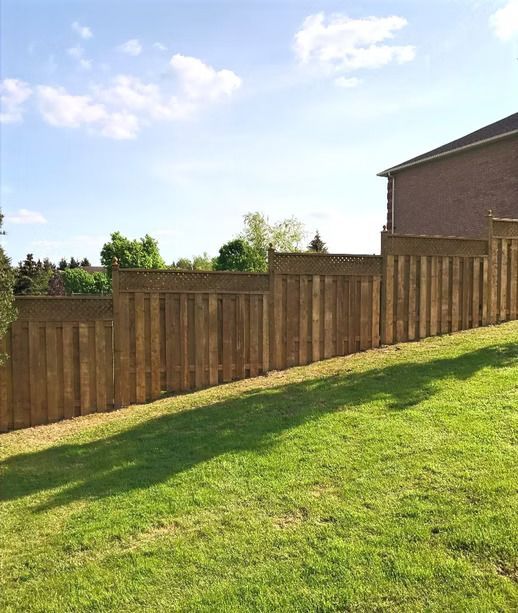 Wooden fence on a slight incline, with green grass in the foreground and a brick building to the right.