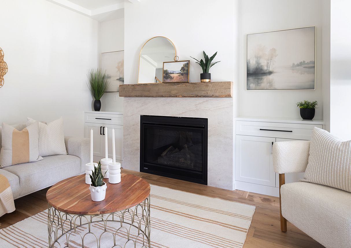 Living room with a fireplace, neutral tones, and plants. Wooden coffee table and rug.