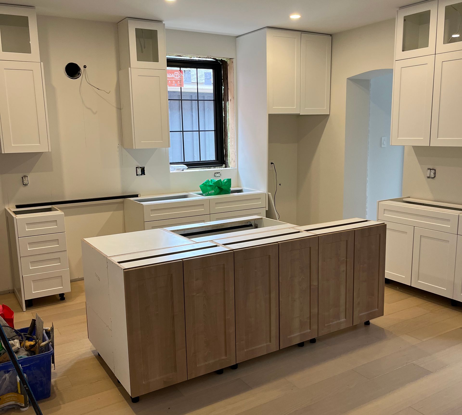Kitchen under construction, with white cabinets, island, and window.