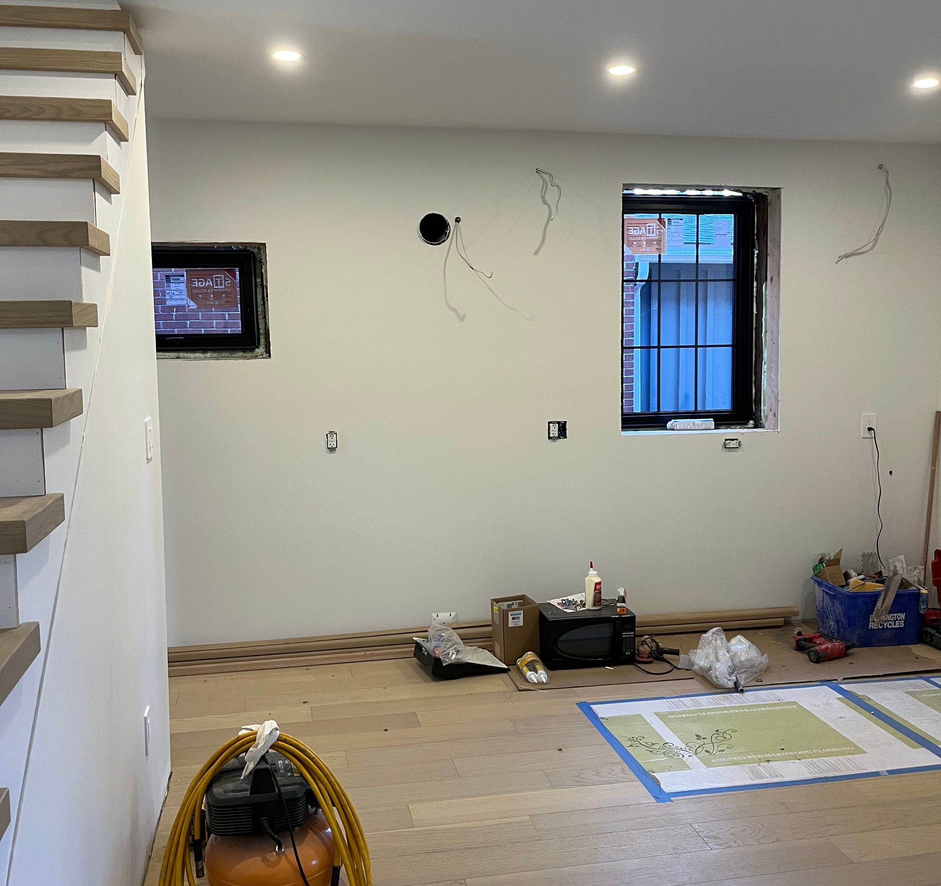 Interior renovation with new hardwood floors, walls, windows, and exposed electrical wires.