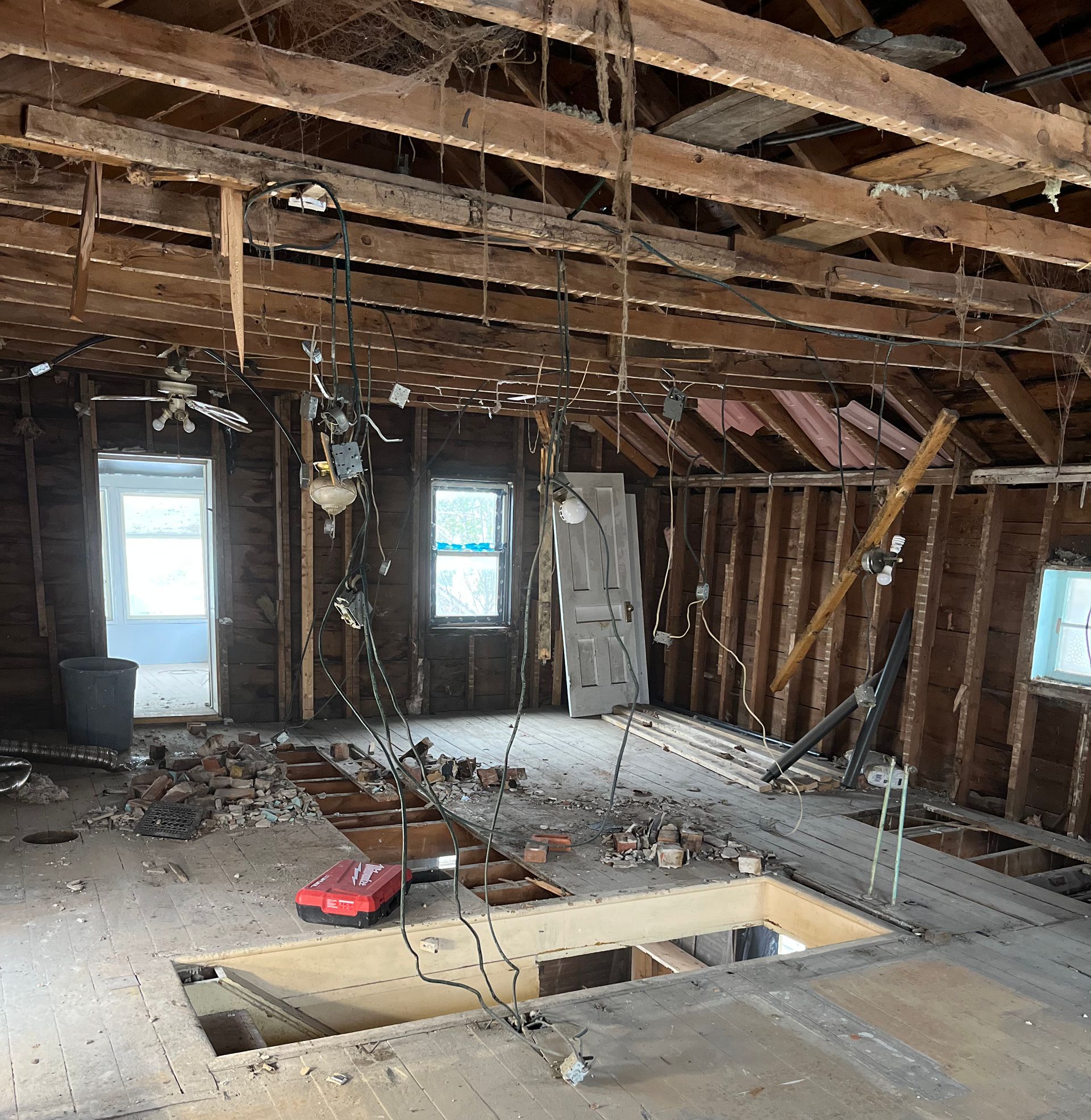 Interior of a room under construction, with exposed beams, walls, and wires hanging down.