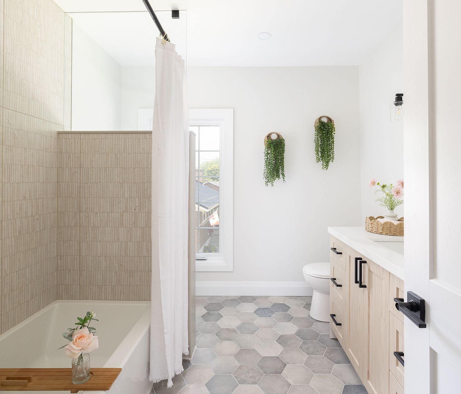 Modern bathroom with light wood vanity, hexagon tile floor, tub, and hanging plants.