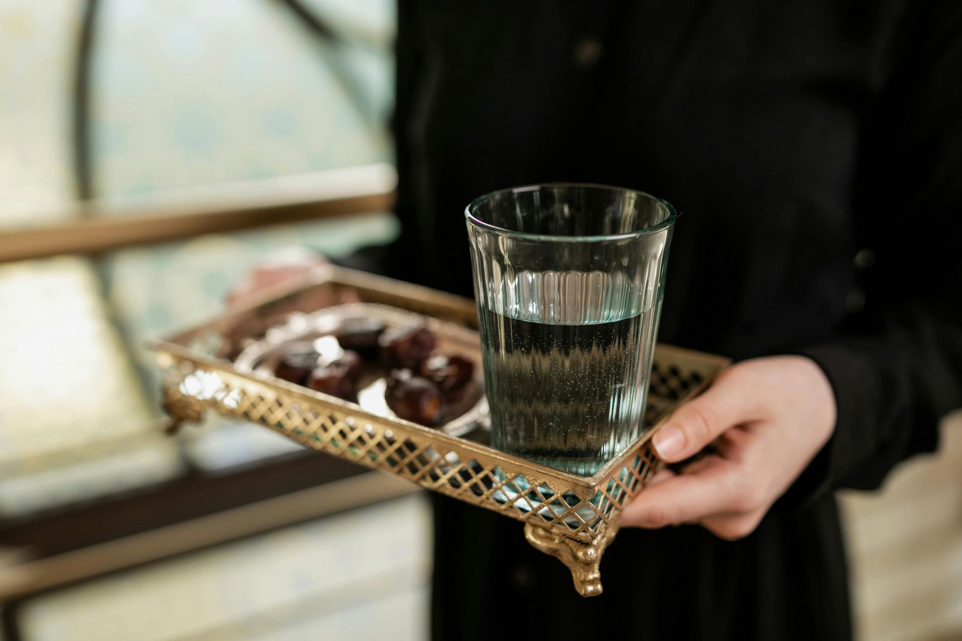 Person holding a tray with dates and a glass of water, likely for breaking a fast.