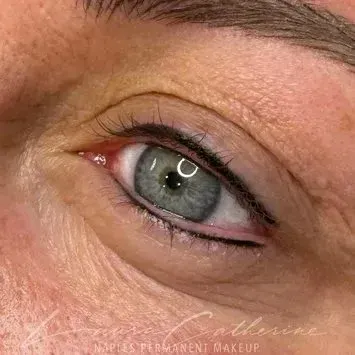 Close-up of eye with permanent eyeliner. Blue-green eye with black eyeliner on the upper and lower lid.