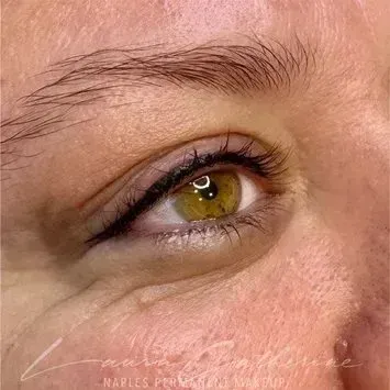 Close-up of an eye with permanent eyeliner; hazel iris, soft skin, subtle eyebrow, and black eyeliner.