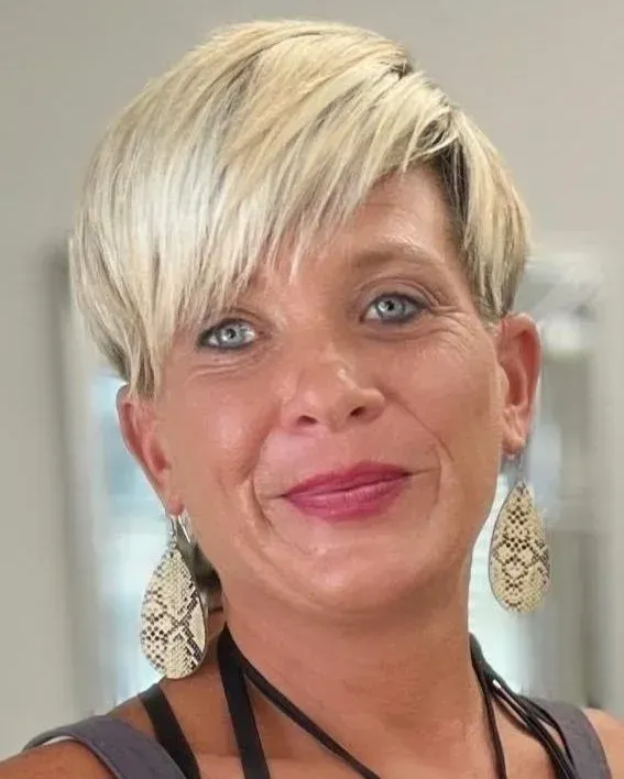 Woman with blonde hair, wearing snake-skin earrings, smiling.