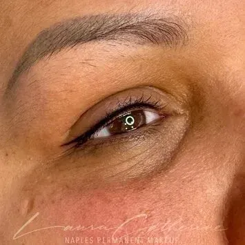 Close-up of a woman's eye with permanent eyeliner and eyebrow makeup. The skin is light brown.