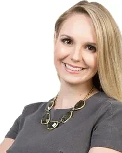 Blonde woman smiling, wearing gray top and statement necklace.