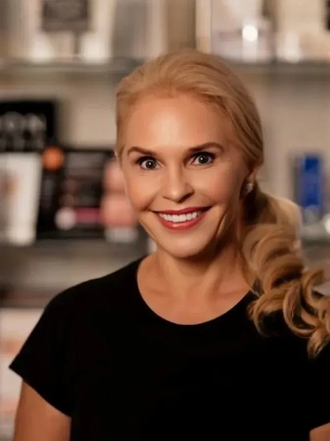 Woman with blonde hair smiles, wearing a black shirt, in a well-lit shop.