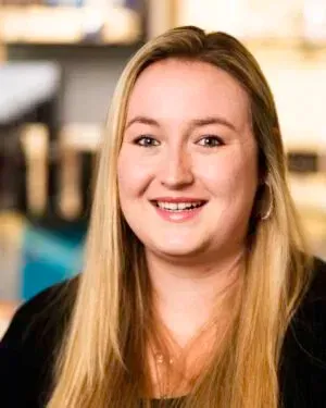 Blonde woman smiles at the camera; long blonde hair, black top, daytime setting.