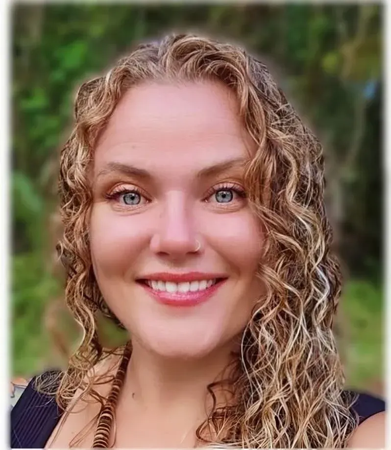 Woman with curly blonde hair, smiling at camera, outdoors.
