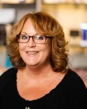 Woman with red hair and glasses smiles, wearing a black shirt.