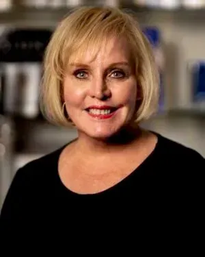 Blonde woman with fair skin and red lipstick smiles, wearing a black shirt.