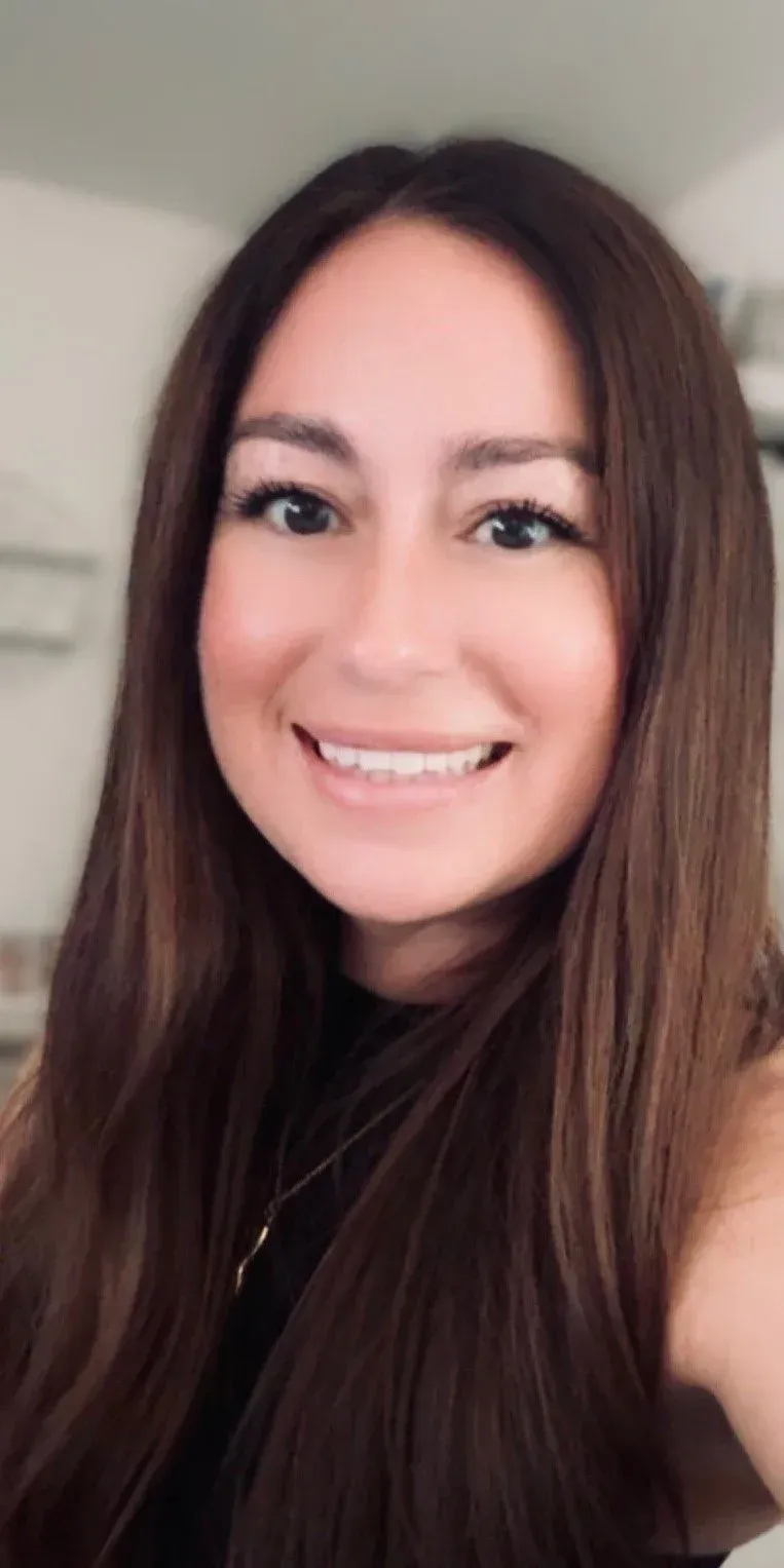 Woman with long brown hair smiles at the camera; wearing a black top.