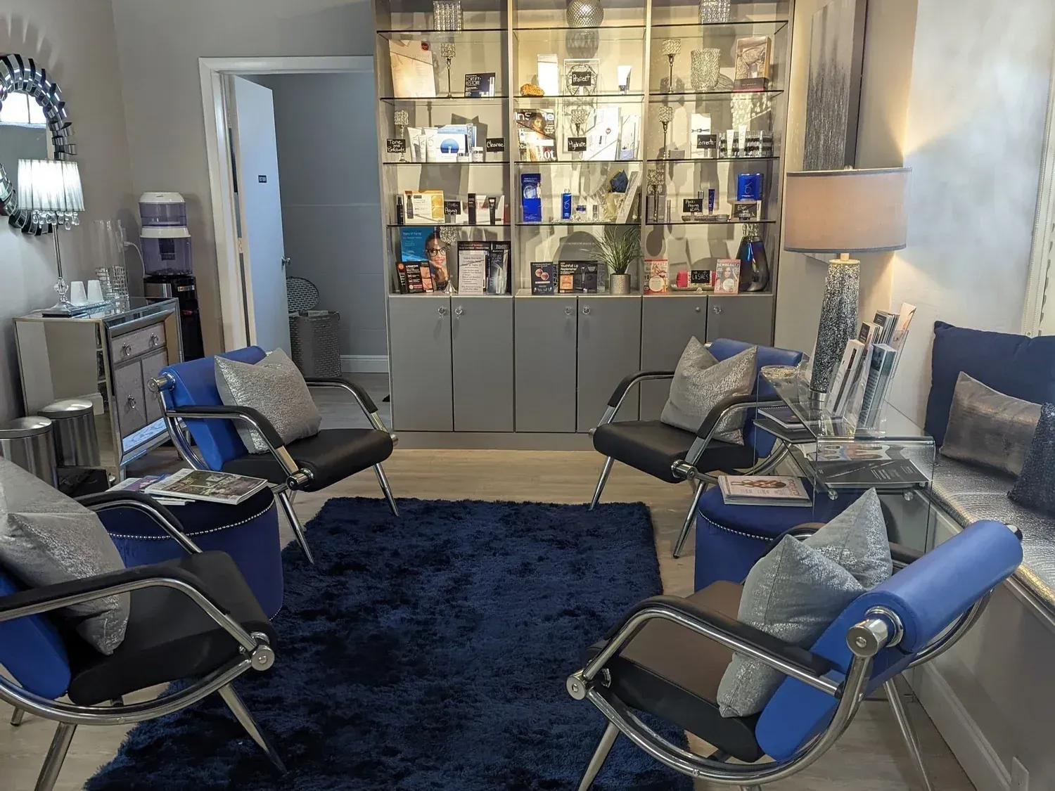 Waiting room with blue chairs, rug, and pillows. Display cabinet and water dispenser.