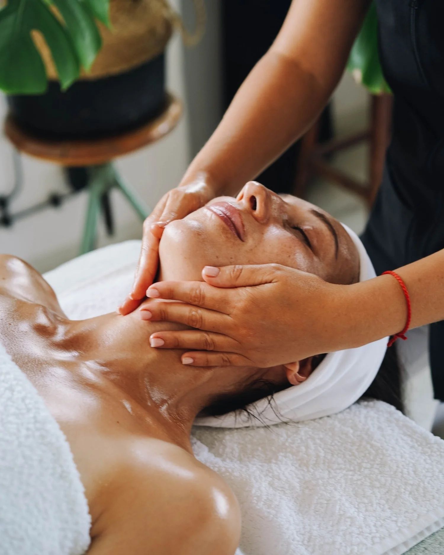 Woman receiving facial massage at a spa, lying on a white towel. Therapist’s hands on face.