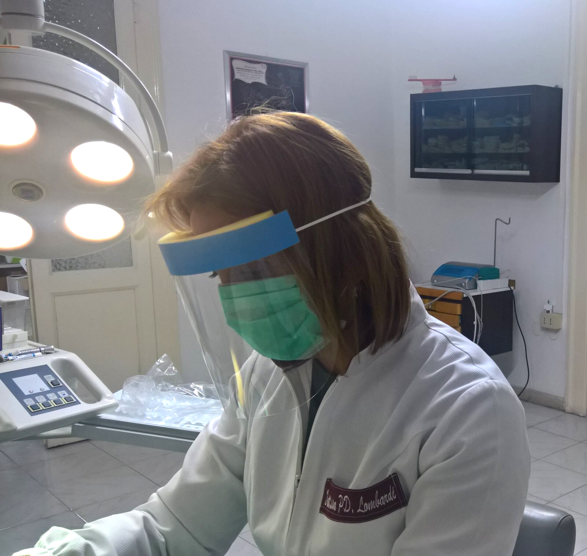 Donna in uno studio dentistico che indossa una mascherina e una visiera protettiva, mentre esamina qualcosa.