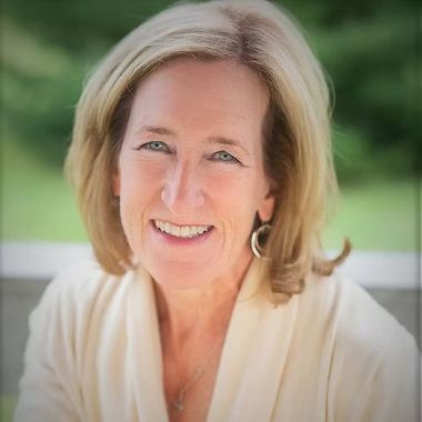 A woman wearing a white sweater and earrings is smiling for the camera.