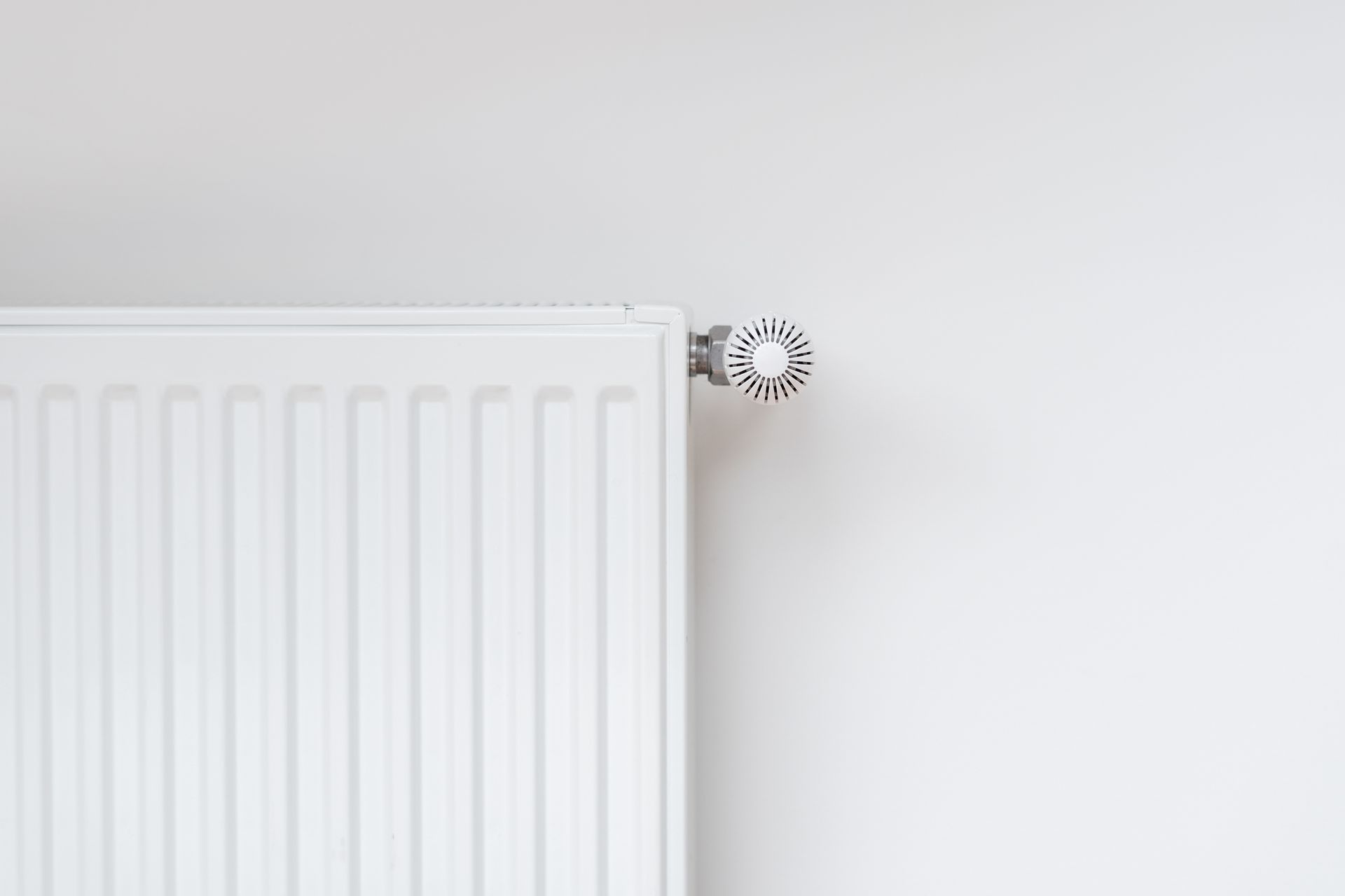 White radiator with a dial on a white wall.