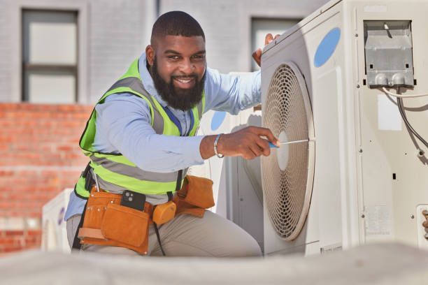 A smiling portrait of a heating and cooling contractor, fixing an AC unit, outdoors.]