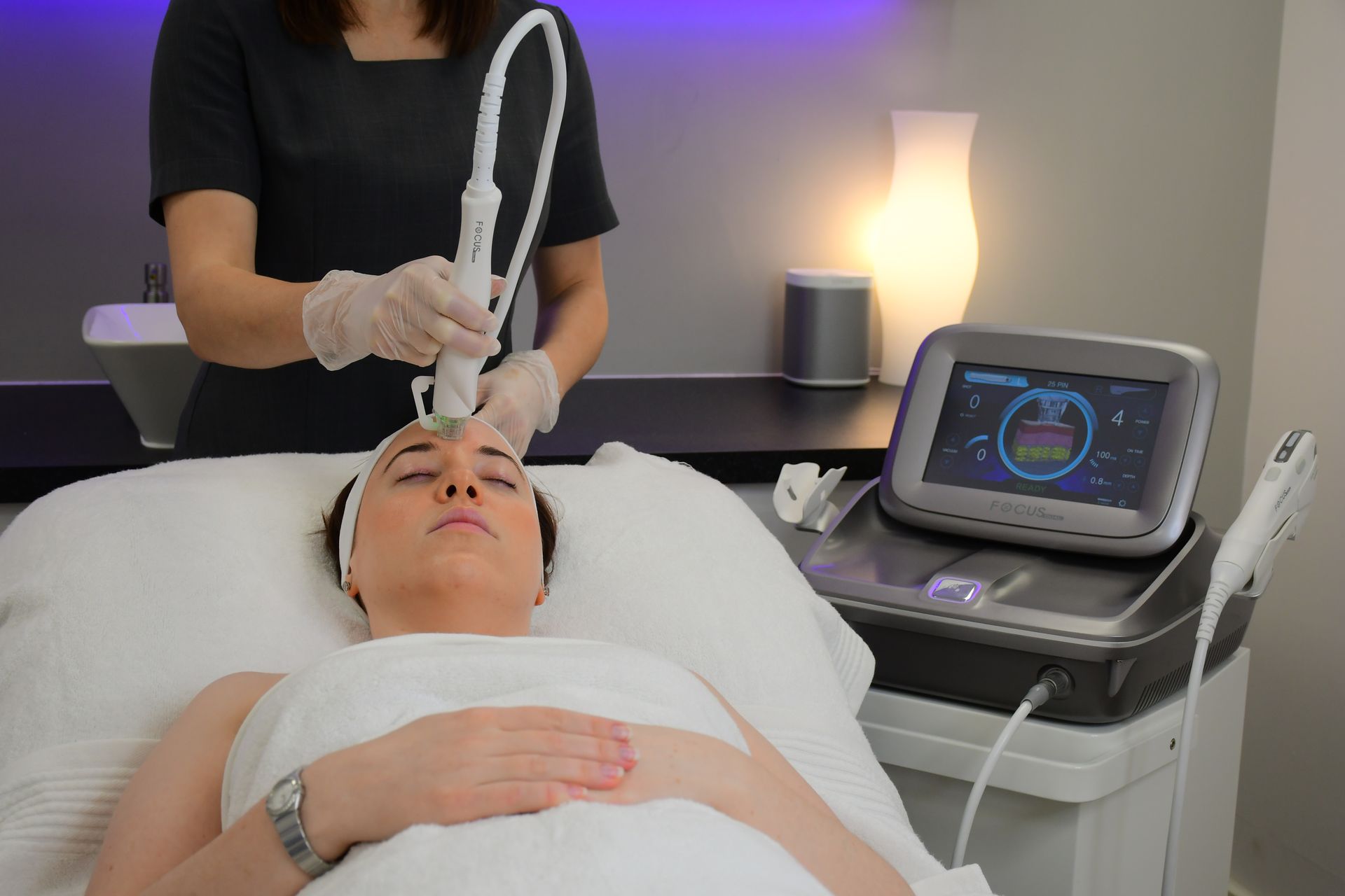 A Therapist performing Radiofrequency Microneedling with the Focus Dual® on the forehead and the Focus Dual® machine in the background