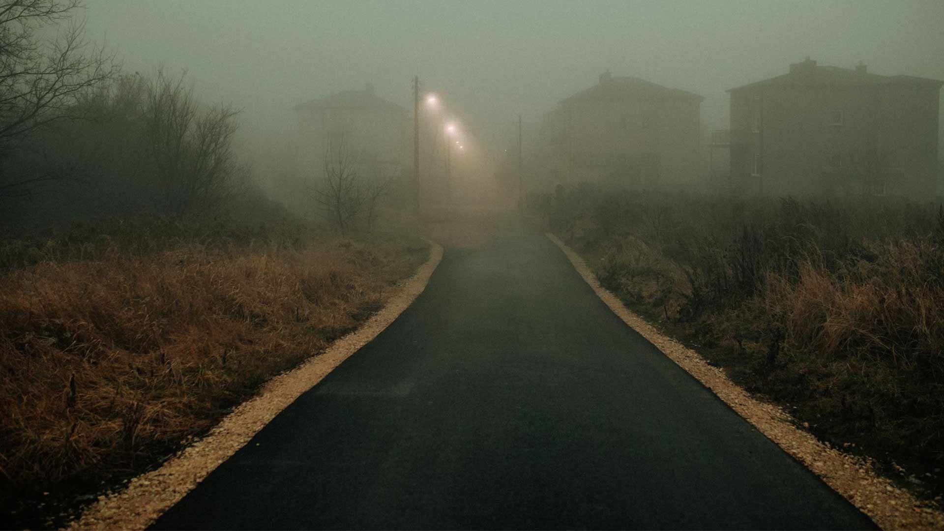 A road going through a foggy field at night.