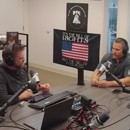 Two men are sitting at a table in front of a flag that says it 's the all of rights