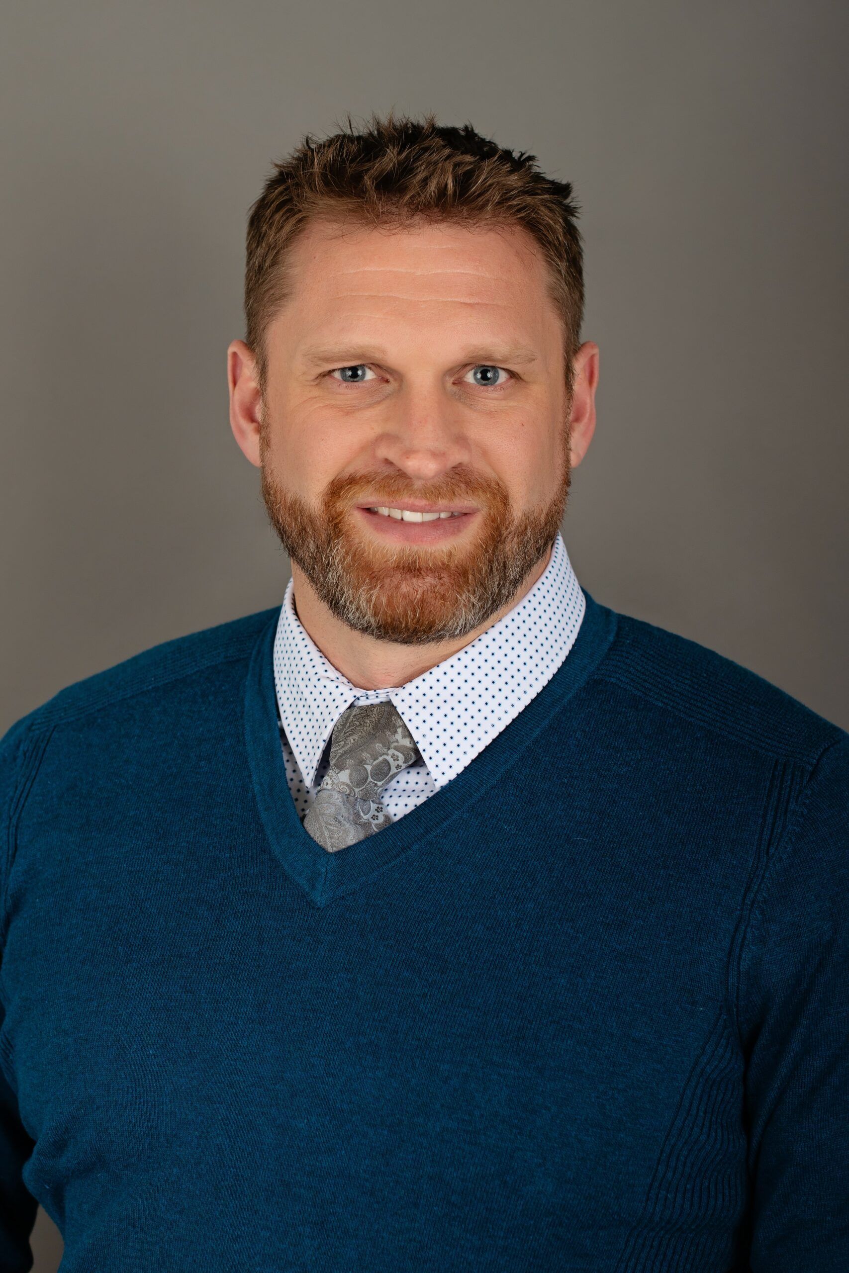 A man with a beard is wearing a blue sweater and tie.