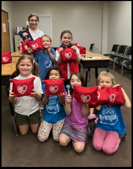 A group of young girls are posing for a picture while holding red pillows with hearts on them